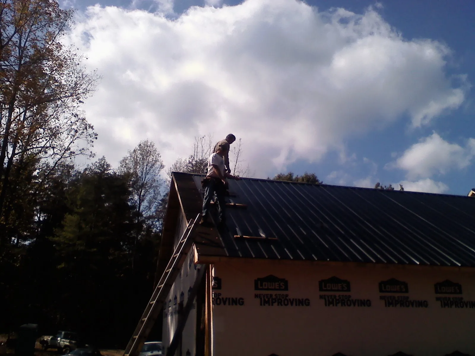 Roofer fastening dark metal panels high against a cloudy sky, from a Roof Inspection job in Middleburg